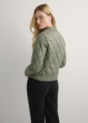 Przejściowa kurtka damska w kolorze khaki KURDT-0564A-55(W26), widok produktu z tyłu na modelce. Widoczna połowa sylwetki.