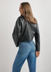 Krótka czarna kurtka skórzana damska KURDS-0597-99(W26), widok produktu z tyłu na modelce. Widoczna połowa sylwetki.