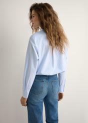 Bawełniana koszula damska w paski KOSDT-0184-7A(W26), widok produktu z tyłu na modelce. Widoczna połowa sylwetki.