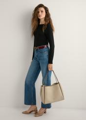 Beżowa torebka shopper damska TOREC-1183-1A(W26) - widok produktu z przodu, trzymanego przez modelkę w ręku, na jasnym tle. Widoczna cała sylwetka. 