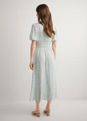 Długa sukienka w kwiaty w kolorze szałwiowym SUKDT-0191-8P(W26), widok produktu z tyłu na modelce. Widoczna cała sylwetka.