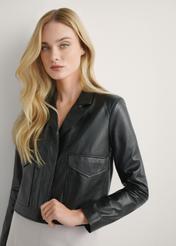Czarna skórzana krótka kurtka damska KURDS-0471-99(W26), zbliżenie na produkt na modelce. Widoczna połowa sylwetki.