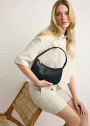 Czarna mała skórzana torebka damska TORES-1263-99(W26) - widok produktu z przodu, trzymanego przez modelkę w ręku, na jasnym tle. Widoczna sylwetka do kolan. 