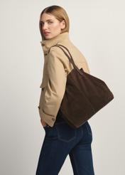 Skórzana ciemnobrązowa torebka damska TORES-1252-1I(W26) - widok produktu po skosie, na modelce, na białym tle. Widoczna sylwetka do kolan.