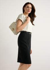 Mała torebka damska w kolorze kremowym TOREC-1186-0B(W26) - widok produktu lekko po skosie, na modelce, na jasnym tle. Widoczna sylwetka do kolan. 