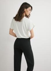 Kremowa bluzka damska BLUDT-0206-0B(W26), widok produktu z tyłu na modelce. Widoczna połowa sylwetki.