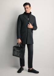 Czarna skórzana teczka męska TORMS-0415A-99(Z25) - widok produktu po skosie, trzymanego przez modela w ręku, na białym tle. Widoczna cała sylwetka. 