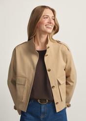 Beżowa przejściowa kurtka damska KURDT-0628-1B(W26) - widok produktu z przodu, na modelce, na jasnym tle. Widoczna połowa sylwetki.