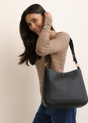 Czarna torebka damska hobo TOREC-1257-9I(Z26), widok skosu produktu, na modelce, na jasnym tle. Widoczna połowa sylwetki. 