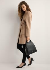 Black women's backpack made of imitation leather TOREC-0923-99(W26), widok produktu w dłoni modelki. Widoczna cała sylwetka.