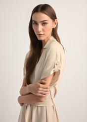 Jasnobeżowa długa sukienka z krótkim rękawem SUKDT-0180A-1A(W26), widok produktu z boku na modelce. Widoczna połowa sylwetki.