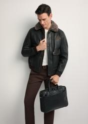 Czarna skórzana torba męska TORMS-0299A-99(Z25)- widok produktu po skosie, trzymanego przez modela w ręku, na białym tle. Widoczna cała sylwetka. 