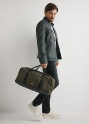 Torba podróżna w kolorze khaki TORMN-0417-8D(W26) - widok produktu z przodu, trzymanego przez modela w ręku, na jasnym tle. 