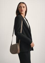 Ciemnobeżowa skórzana półokrągła torebka listonoszka TORES-0972F-1K(W26), widok produktu skosem na modelce, widoczna połowa sylwetki.