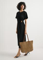 Słomkowa torebka shopper TOREC-1218-1E(W26) - widok produktu lekko po skosie, trzymanego przez modelkę w ręku, na jasnym tle. Widoczna cała sylwetka. 