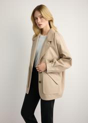 Beżowa skórzana kurtka damska oversize KURDS-0577-1B(W26) - widok produktu z boku, na modelce, na jasnym tle. Widoczna sylwetka do kolan. 