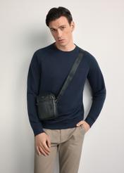 Czarna skórzana saszetka męska z logo TORMS-0296A-99(Z25) - widok produktu po skosie, na modelu, na białym tle. Widoczna sylwetka do kolan.