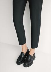 Czarne skórzane loafersy damskie BUTYD-1069-99(W26) - widok produktu z przodu, na modelce, na jasnym tle. Widoczna sylwetka do kolan. 