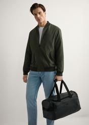 Czarna torba podróżna TORMN-0412-99(W26), widok produktu w ręce modela. Widoczna cała sylwetka.