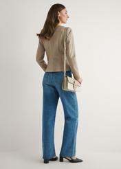 Kremowa torebka listonoszka damska TOREC-1120-0P(W26) - widok produktu lekko po skosie, na modelce, na jasnym tle. Widoczna cała sylwetka. 