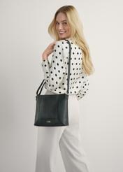 Czarna skórzana torebka damska TORES-1265-9I(W26) - widok produktu z przodu, na modelce, na jasnym tle. Widoczna sylwetka do kolan. 