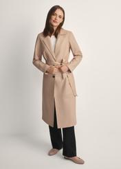 Beżowy skórzany płaszcz damski KURDS-0613-1B(W26) - widok produktu na modelce z przodu, na jasnym tle. Widoczna cała sylwetka. 