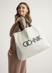 Bawełniana torba w kolorze ecru TOREN-0136-1E(W26) - widok produktu z przodu, na modelce, na jasnym tle. Widoczna sylwetka do połowy.
