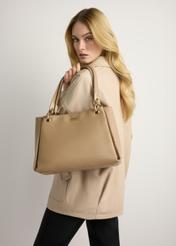 Beżowa damska torebka z imitacji skóry TOREC-0998-1D(W26) - widok produktu z przodu, trzymanego przez modelkę w ręku, na jasnym tle. Widoczna sylwetka do kolan.