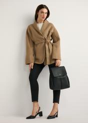 Czarny średni plecak damski TOREC-1132-99(W26) - widok produktu   z przodu, trzymanego przez modelkę w ręku, na jasnym tle. Widoczna cała sylwetka. 