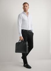 Czarna skórzana torba na laptopa TORMS-0494-99(W26) - widok produktu lekko po skosie, trzymanego przez modela w ręku, na jasnym tle. 