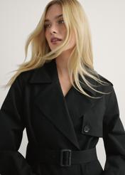 Długa czarna kurtka damska w formie płaszcza KURDT-0512-99(W25), widok produktu od przodu na modelce, widoczna połowa sylwetki.