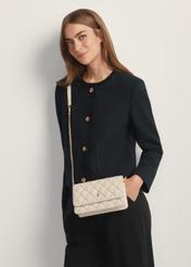 Mała pikowana torebka damska w kolorze kremowym TOREC-1150-0B(W26) - widok produktu z przodu, na modelce, na jasnym tle. Widoczna sylwetka do połowy.