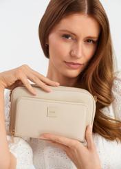 Mała beżowa torebka damska na ramię TOREC-0904A-80(W25)- widok modelki trzymającej produkt w ręku na białym tle. 
