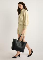 Czarna torebka shopper z monogramem TOREC-1181-99(W26) - widok produktu z przodu, na modelce, na jasnym tle. Widoczna cała sylwetka. 