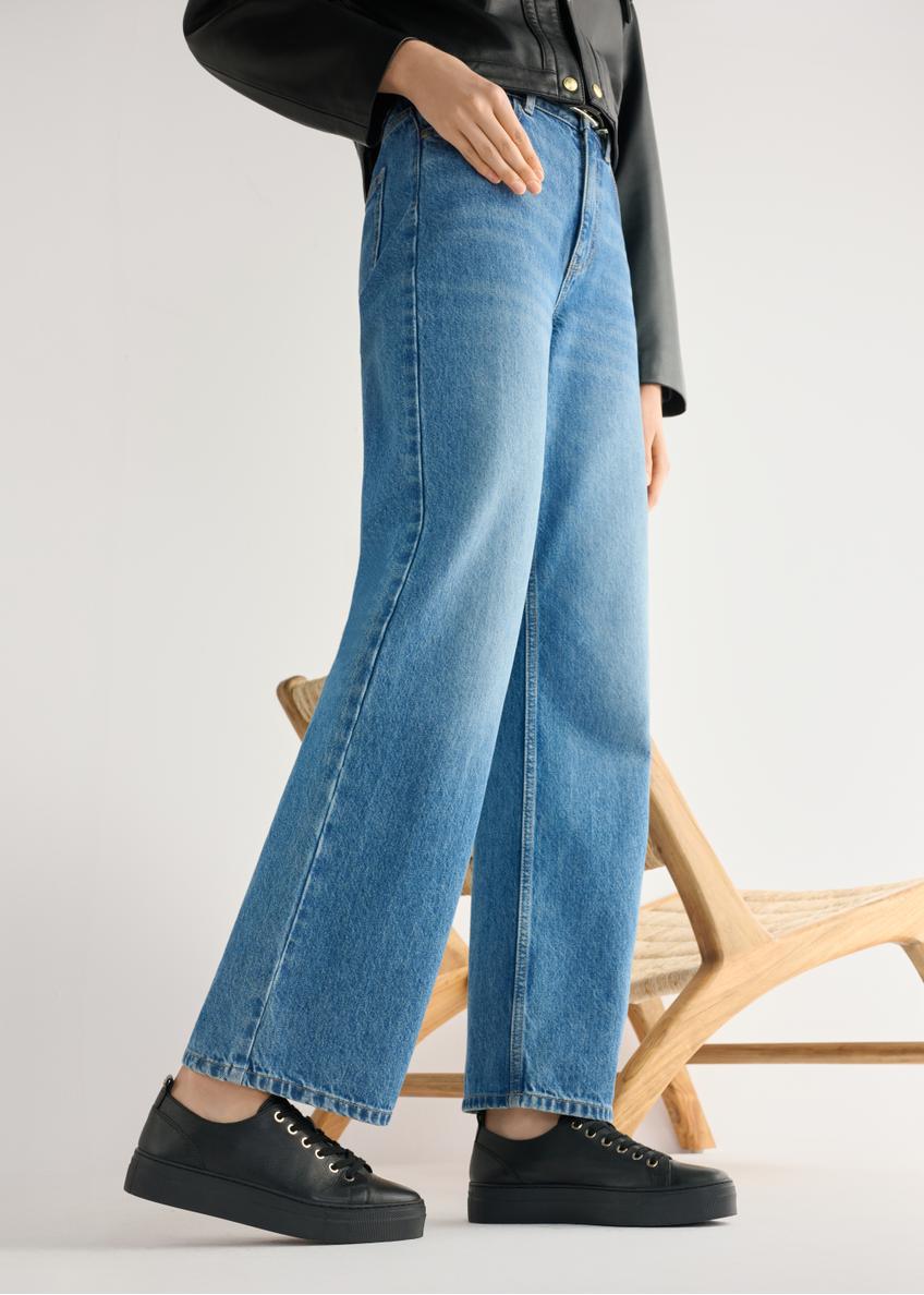 Wysokie czarne skórzane tenisówki damskie BUTYD-1062-99(W26) - widok produktu z boku, na modelce, na jasnym tle. Widoczna sylwetka do kolan. 