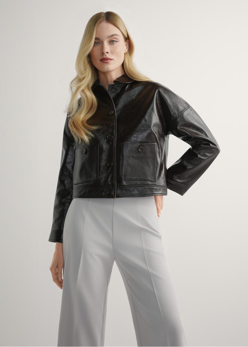 Brązowa skórzana krótka kurtka damska KURDS-0593-1I(W26) - widok produktu z przodu, na modelce, na jasnym tle. Widoczna sylwetka do kolan. 