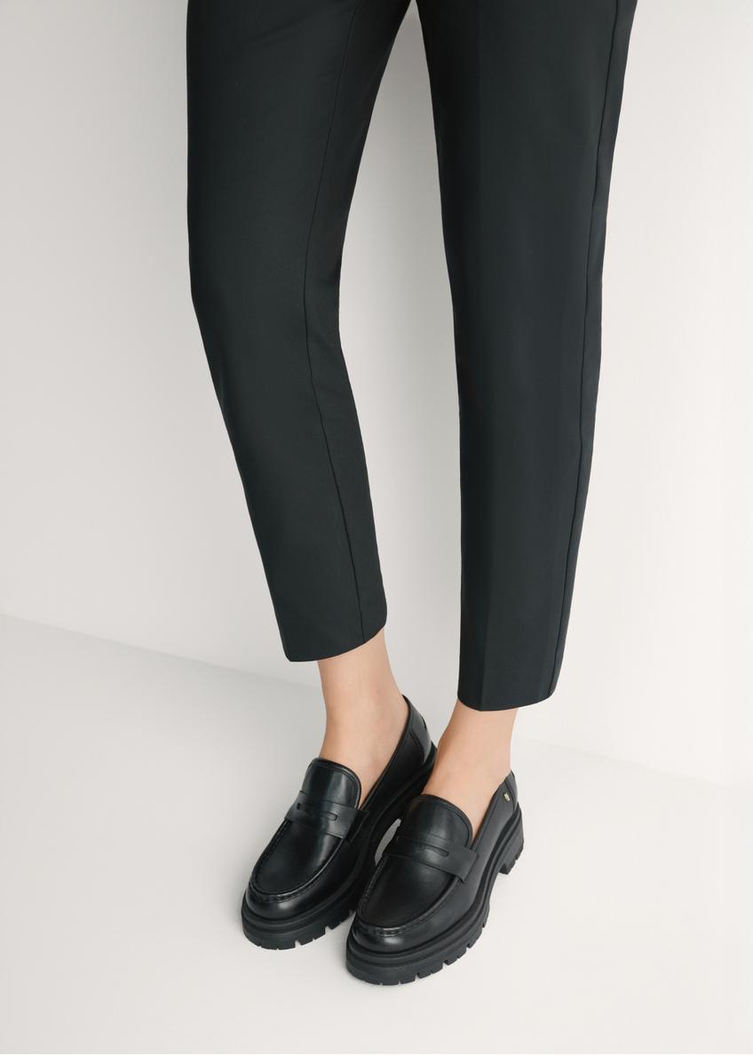 Czarne skórzane loafersy damskie BUTYD-1069-99(W26) - widok produktu z przodu, na modelce, na jasnym tle. Widoczna sylwetka do kolan. 